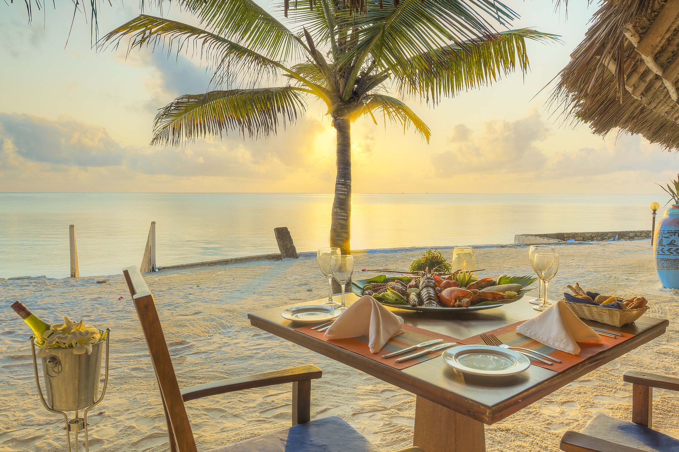 Candle-lit dinner table set on the beach at sunset